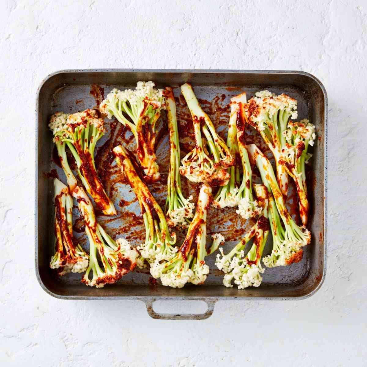 Raw cauli-blossom florets in a large roasting tray tossed in seasoning. 