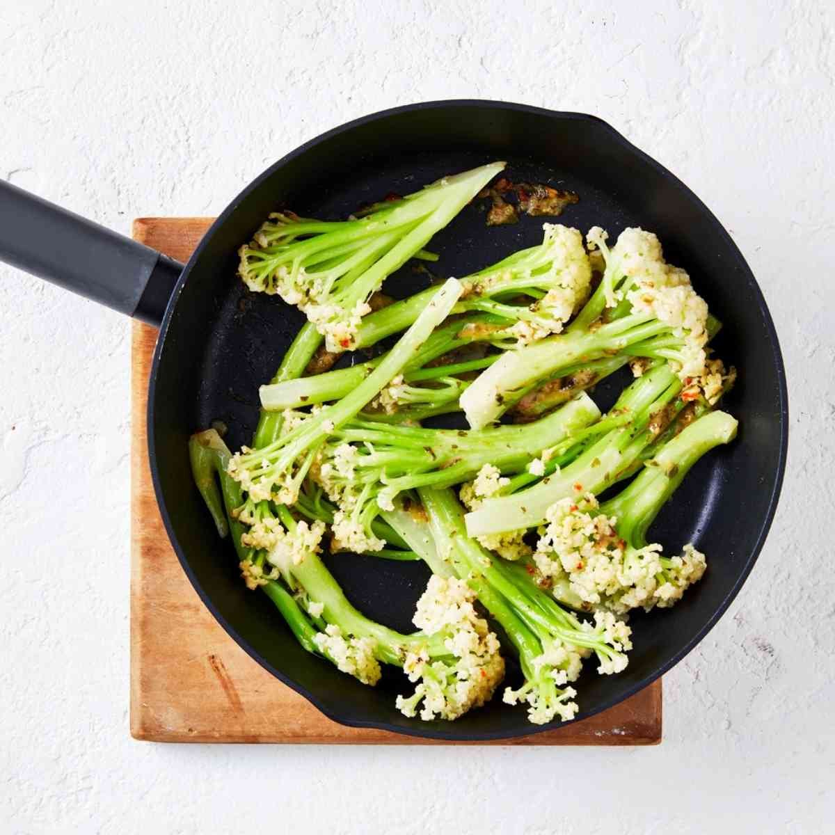 Raw cauliblossom florets in a large black frying pan topped with seasoning paste.