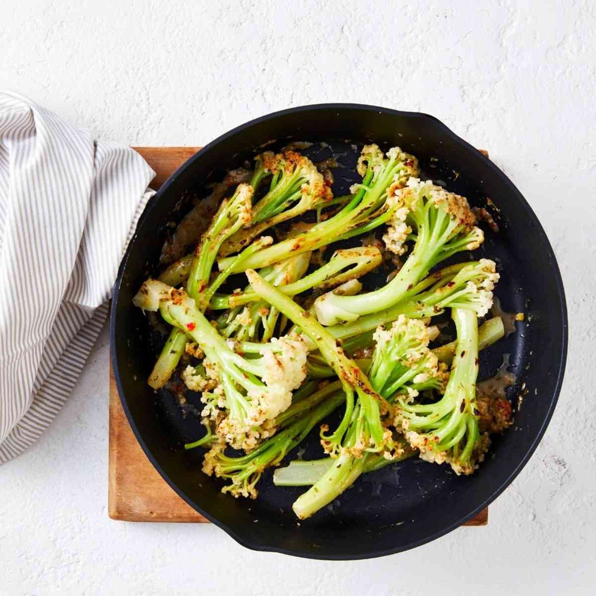 Cooked cauliblossom florets in a large black frying pan topped with seasoning paste.