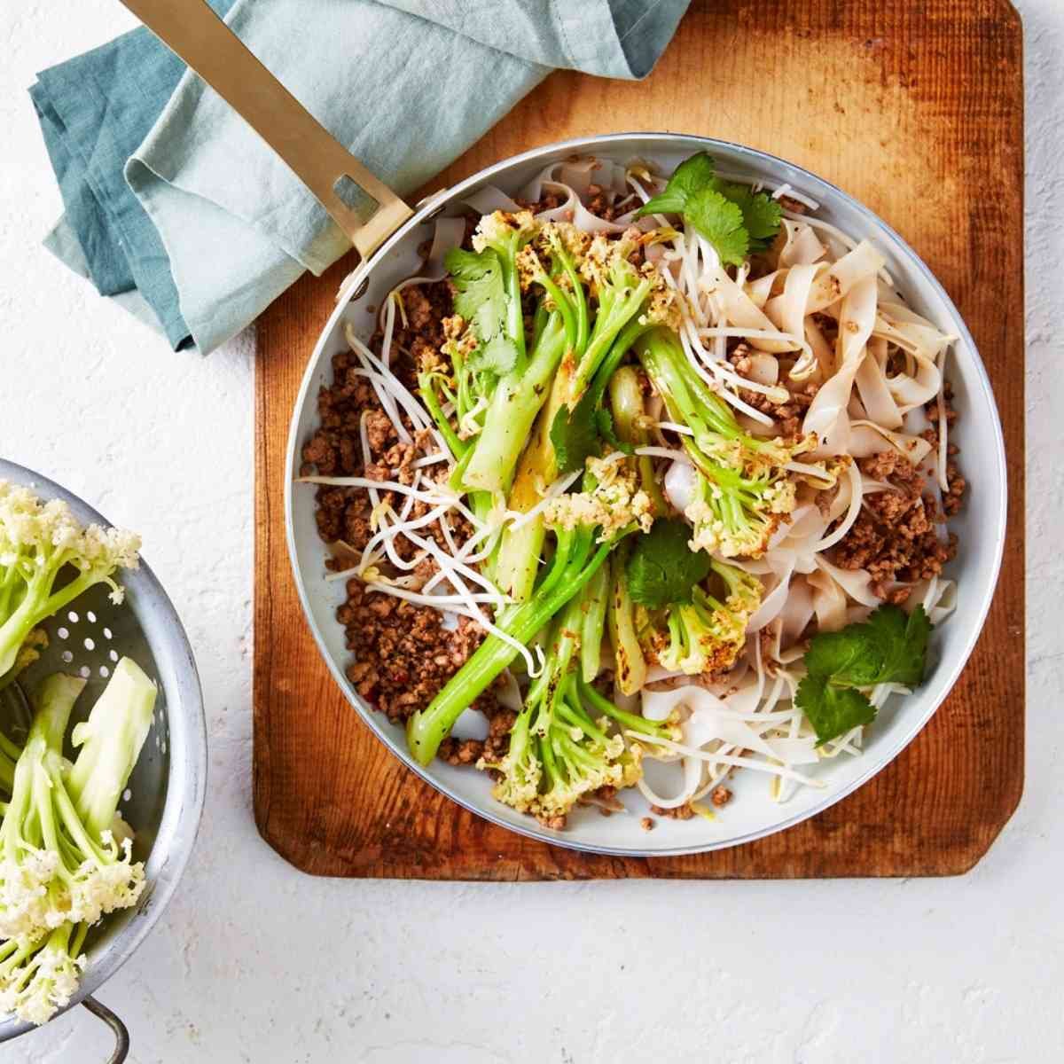 A frying pan with pork mince, noodles, and cauliblossom florets on top. 